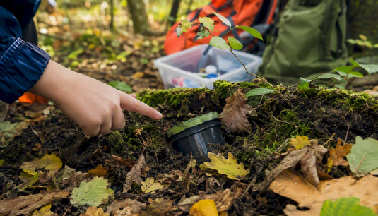 Kind zeigt auf einen kleinen Geocache im Wald