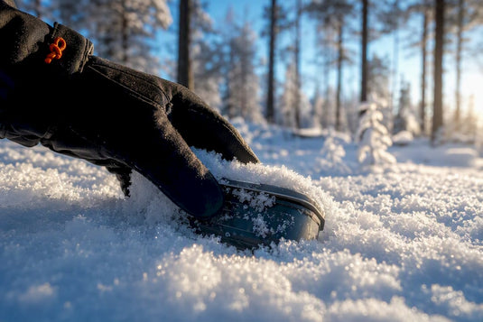 Eine Hand befreit vorsichtig einen verschneiten Cache
