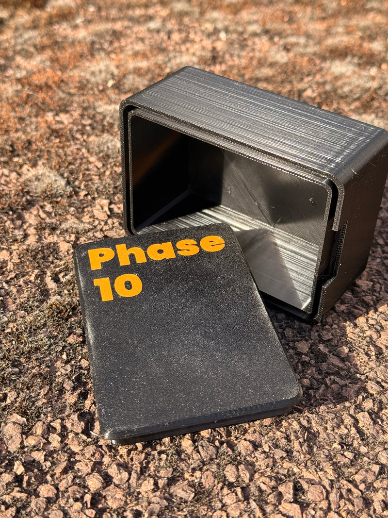 Laden Sie das Bild in Galerie -Viewer, Offene CacheWerk GameBox für Phase 10 mit abgenommenem Deckel und orangefarbener Beschriftung
